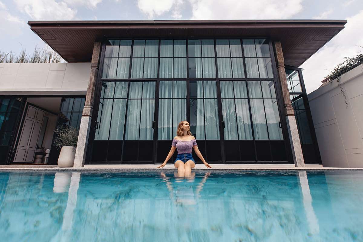 Young model sitting by a pool in a bright luxury backyard