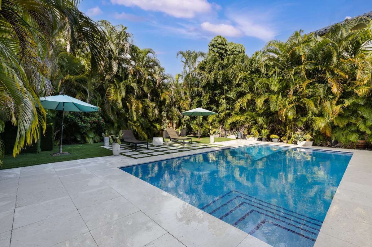Modern backyard with swimming pool, artificial grass, stone path, trees, and chairs