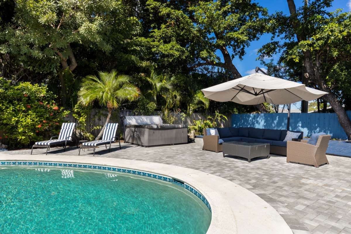 Modern backyard with pool, artificial grass, stone path, trees, and patio chairs