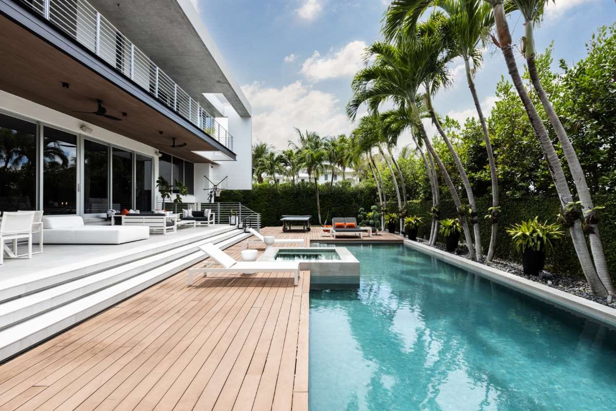Modern backyard with swimming pool, artificial grass, stone path, trees, and patio chairs