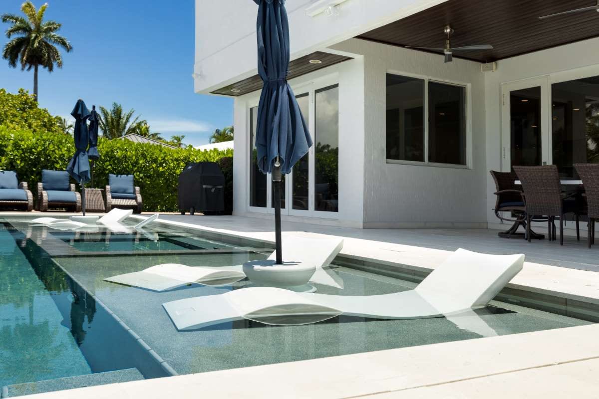 Modern backyard with pool, artificial grass, stone path, trees, and patio chairs