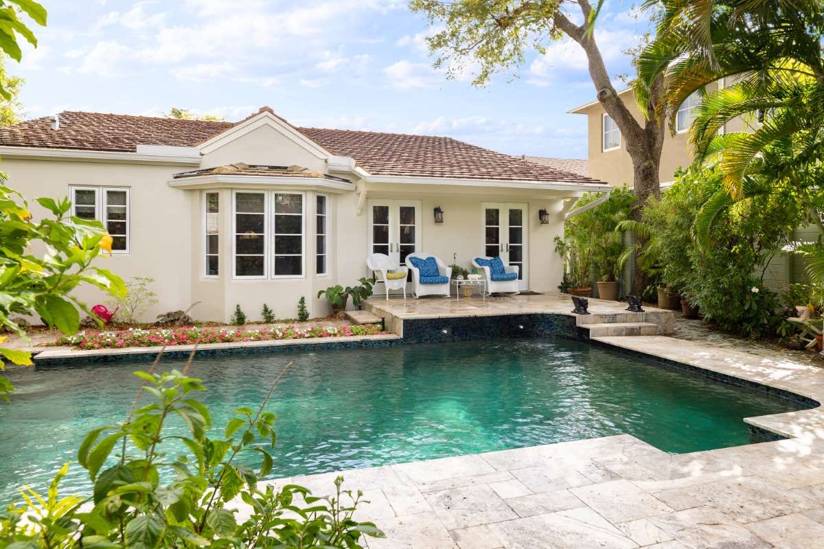 Modern backyard with pool, stone path, artificial grass, trees, and patio chairs