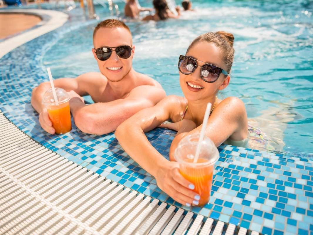 Couple relaxing by a resort pool with cocktails and umbrellas