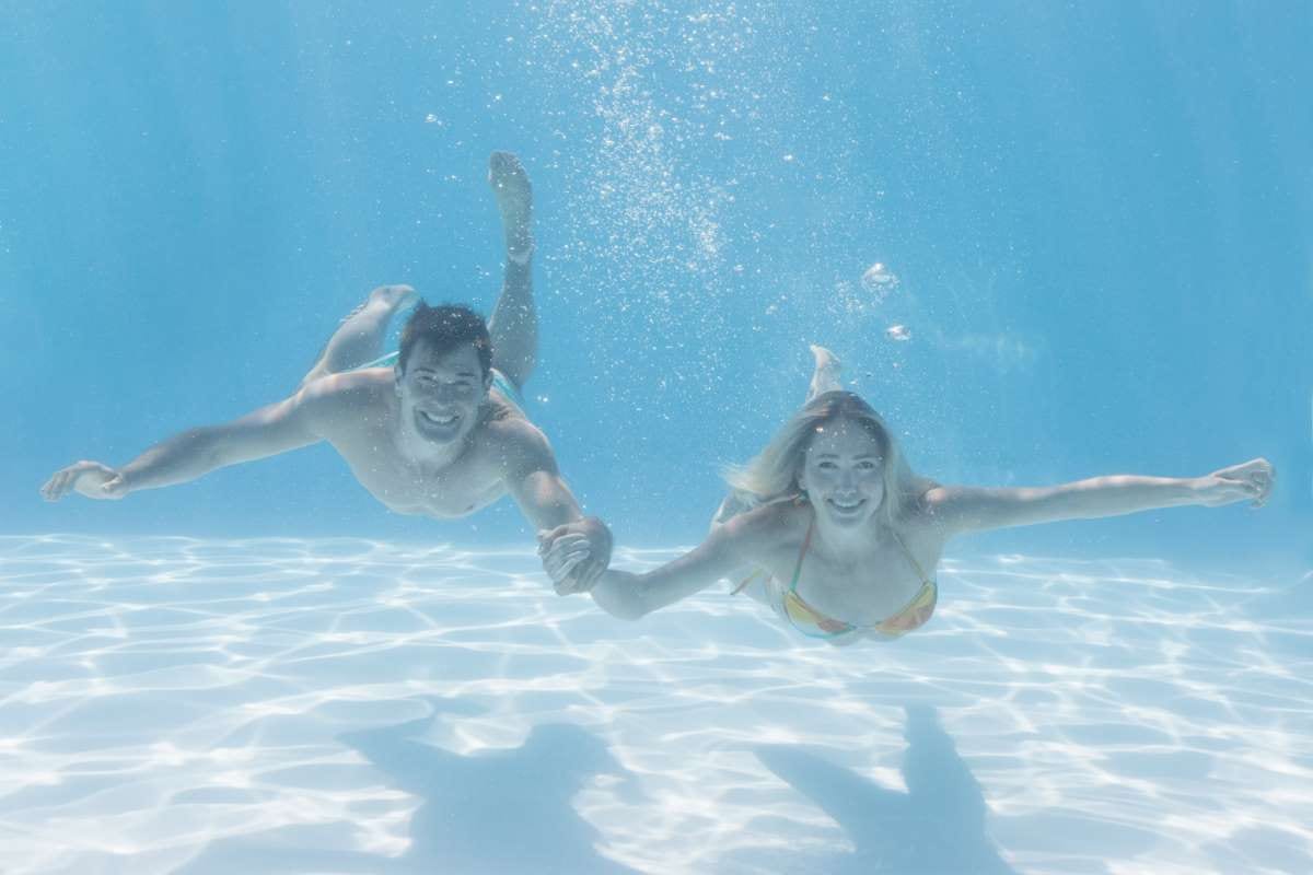 Cute couple smiling at camera underwater in a swimming pool