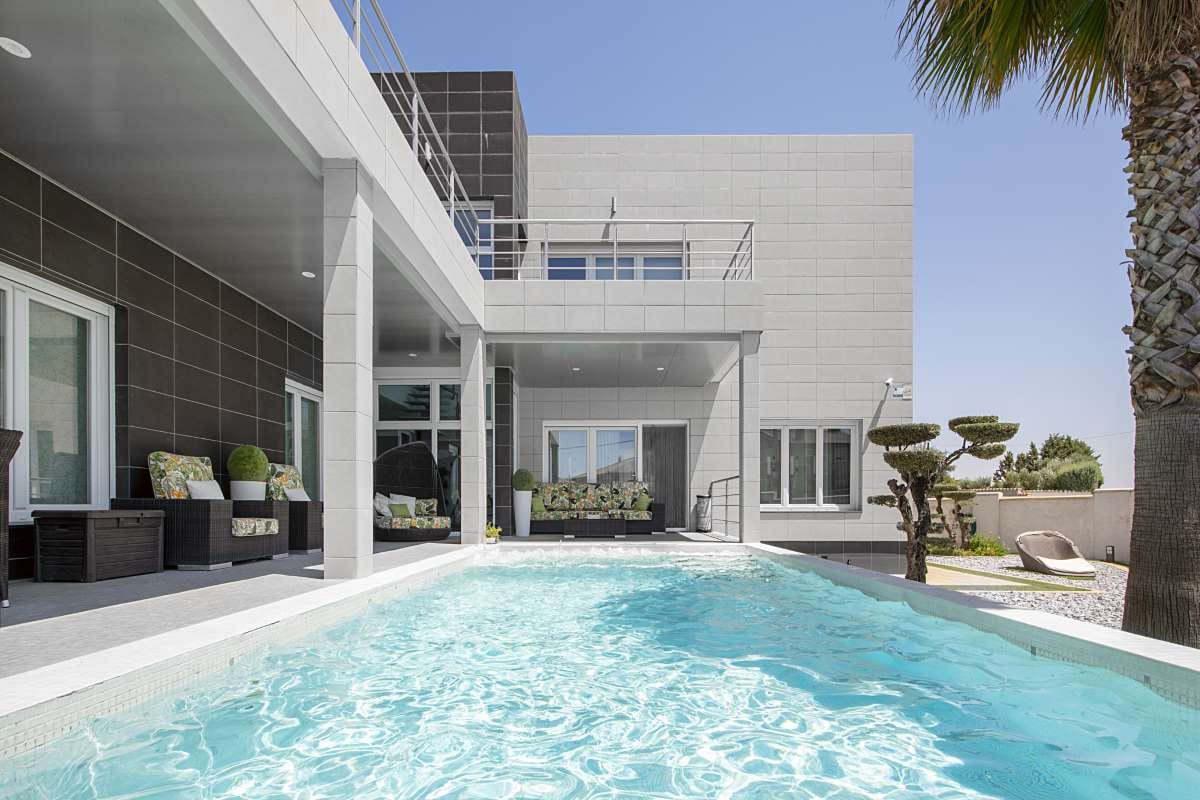 Modern detached house with pool, palm trees, porch seating, and minimalist landscaping