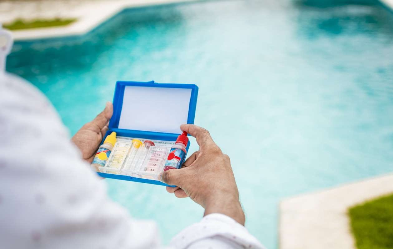 Hand holding a pool water test kit with a blurred pool in the background