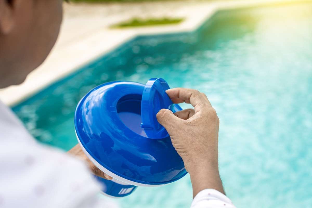 Worker holding a pool chlorine dispenser with gloved hands