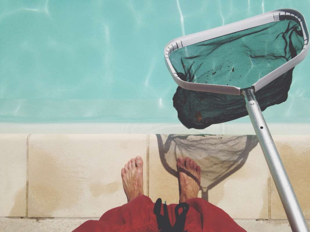 Person holding a fishing net by a swimming pool