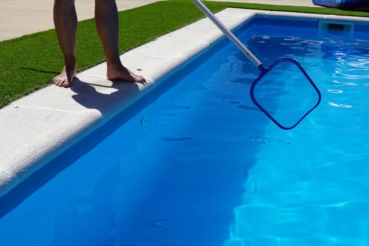 Pool technician cleaning the pool surface with a mesh skimmer