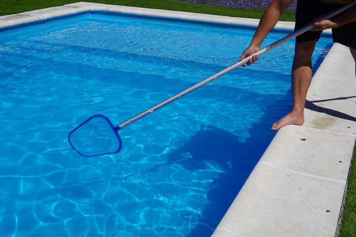 Man cleaning a pool surface with a mesh skimmer