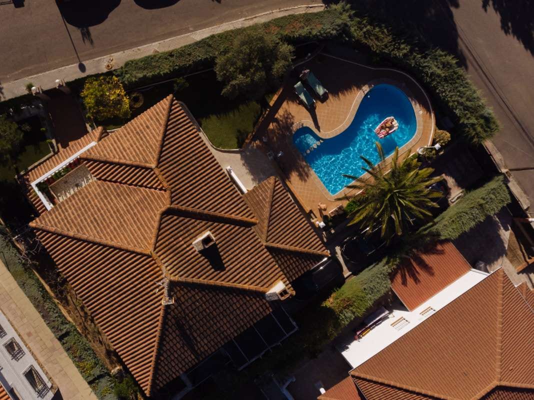 Man floating on a mattress in a swimming pool beside a villa house
