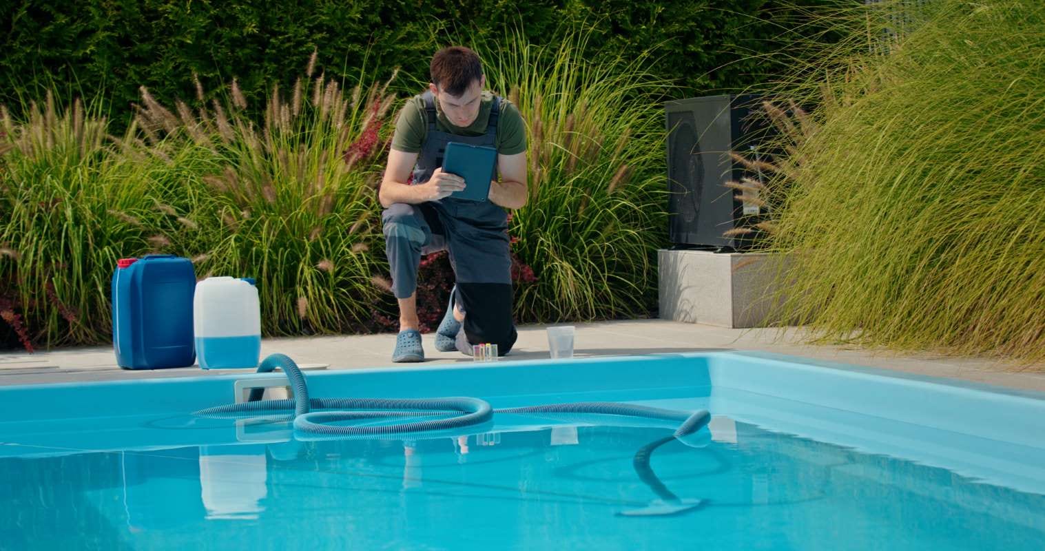 Pool technician using a tablet by the pool with chemical containers nearby
