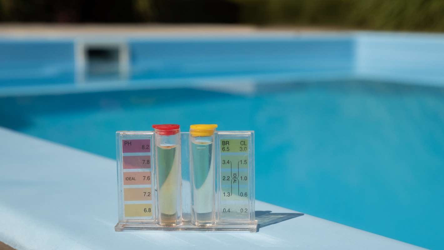 Pool water testing kit with pH and chlorine levels beside a blue pool