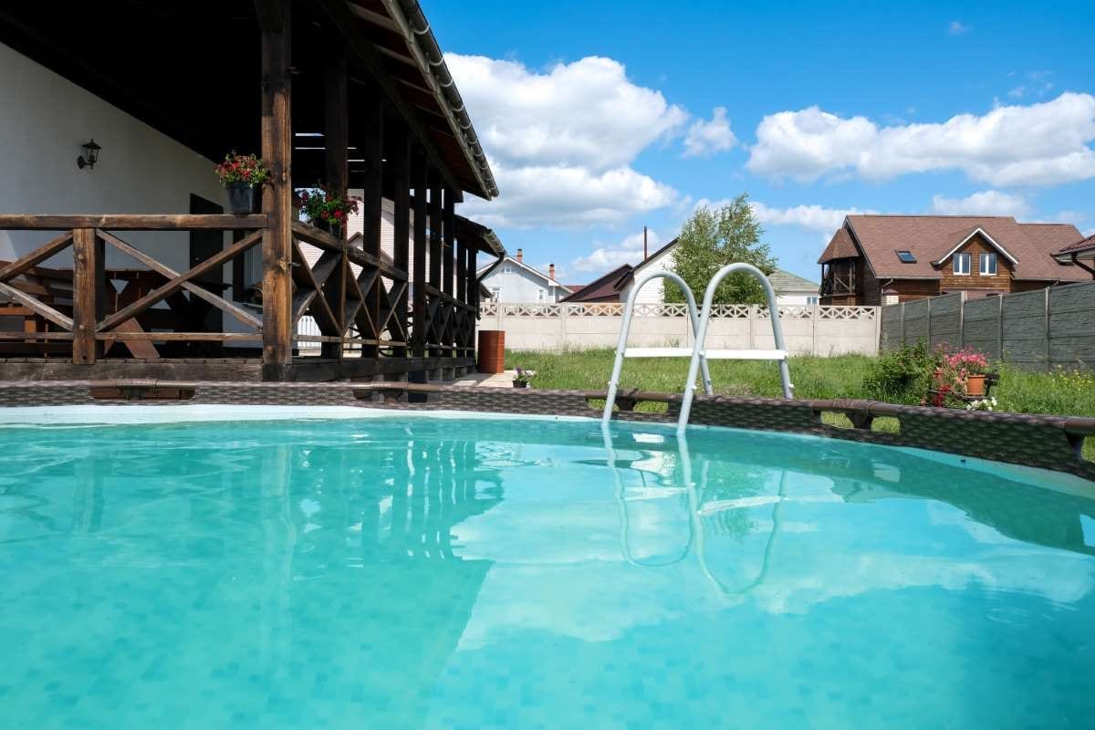 Private blue-frame swimming pool beside a house on a sunny summer day