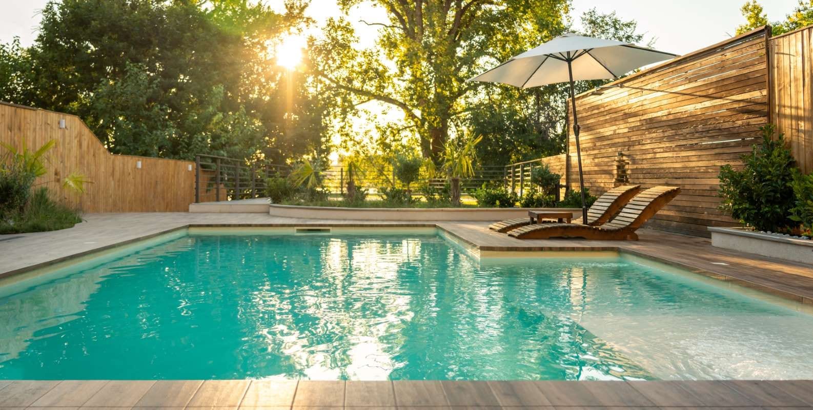 Sunset view of a luxury villa pool with wooden lounge chairs, evoking calm and opulence