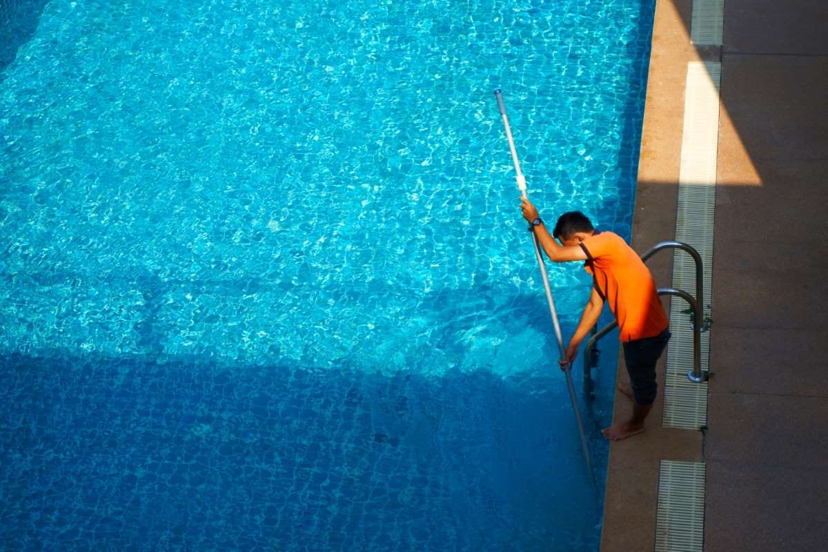 Worker cleaning a private swimming pool from above on a summer day