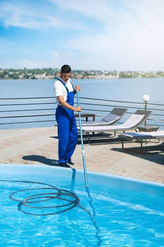 Worker cleaning an outdoor swimming pool with an underwater vacuum